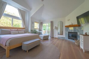 Une chambre avec un grand lit, un canapé, une cheminée et une vue sur la verdure environnante.
