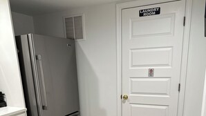 A compact kitchen with a stainless steel refrigerator, a white door labeled "Laundry Room," and a round table with two black placemats and a small wooden object on it. - Charming 1-bedroom, 1 bathroom townhome in awesome Baltimore with WiFi, AC (Baltimore)