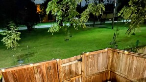 A wooden deck with a white railing, a stone bench, and a view of a green lawn and trees. - Charming 1-bedroom, 1 bathroom townhome in awesome Baltimore with WiFi, AC (Baltimore)