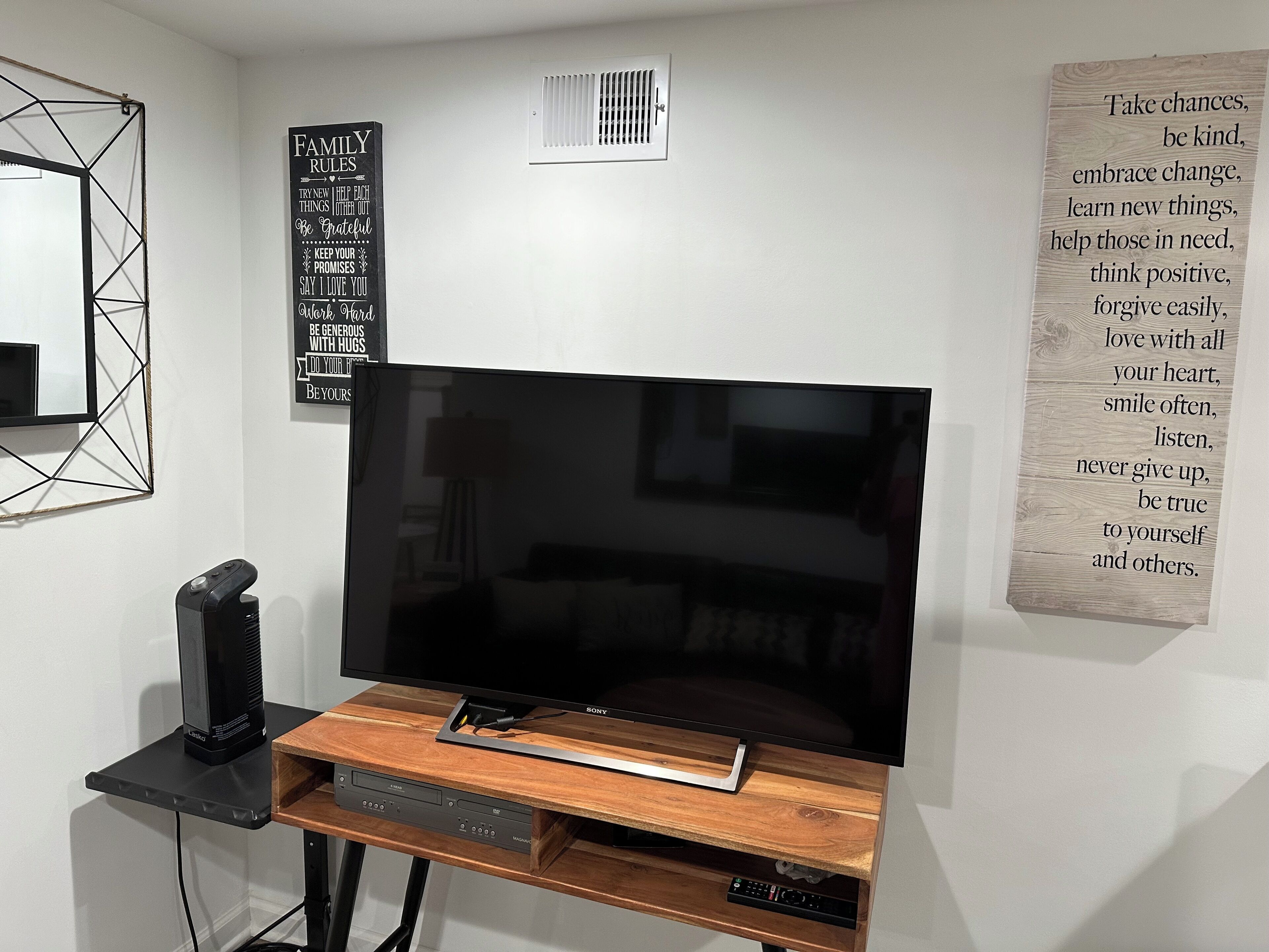 Una sala de estar moderna con una televisión de pantalla plana sobre un soporte de madera, un altavoz y una pared con citas motivacionales.