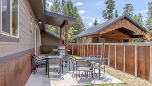 A wooden cabin with a patio area featuring metal chairs and a grill.