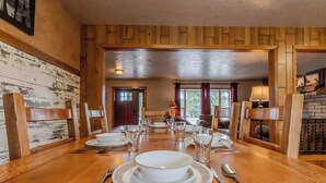 A wooden dining table set with plates, bowls, and cutlery, flanked by wooden chairs.