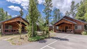 Two wooden cabins with large windows, a covered porch, and a parking area.