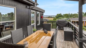 Une terrasse extérieure couverte, équipée d’une table et de chaises, d’un barbecue et offrant une vue sur les environs.