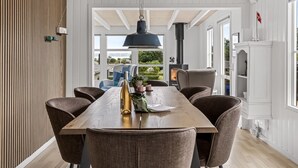 Un espace repas comprenant une longue table, six chaises, un luminaire suspendu et une vue sur l’extérieur.