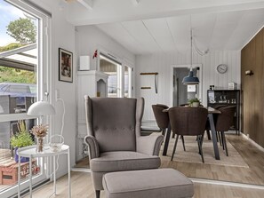 A modern interior with a grey upholstered armchair, a dining table with chairs, and a pendant light.