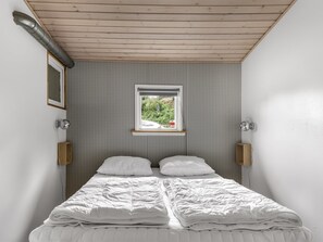 A bedroom with a bed, a window, and a wall-mounted light fixture.
