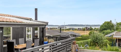 A modern outdoor seating area with a wooden deck, a barbecue grill, and a view of a lake and residential buildings in the background.