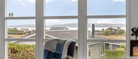 A room with a large window overlooking a residential area, a chair, and a couch.