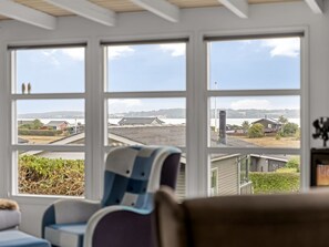 A room with a large window overlooking a residential area, a chair, and a couch.
