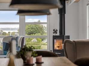 A room with a large window, a black heater, and a view of greenery outside.