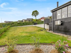 A residential property with a well-maintained lawn, a garden with various plants, a modern building with large windows, and a visible chimney.