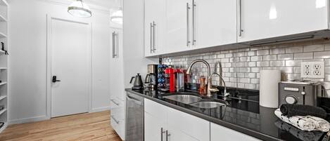 A modern kitchen with white cabinets, a black countertop, and a wooden floor.