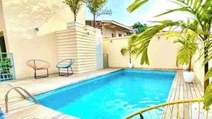 Une piscine avec une terrasse en bois, deux chaises longues et un palmier.