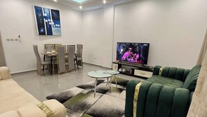 Un salon moderne avec un canapé vert, un canapé beige, une table à manger avec des chaises et un téléviseur à écran plat.