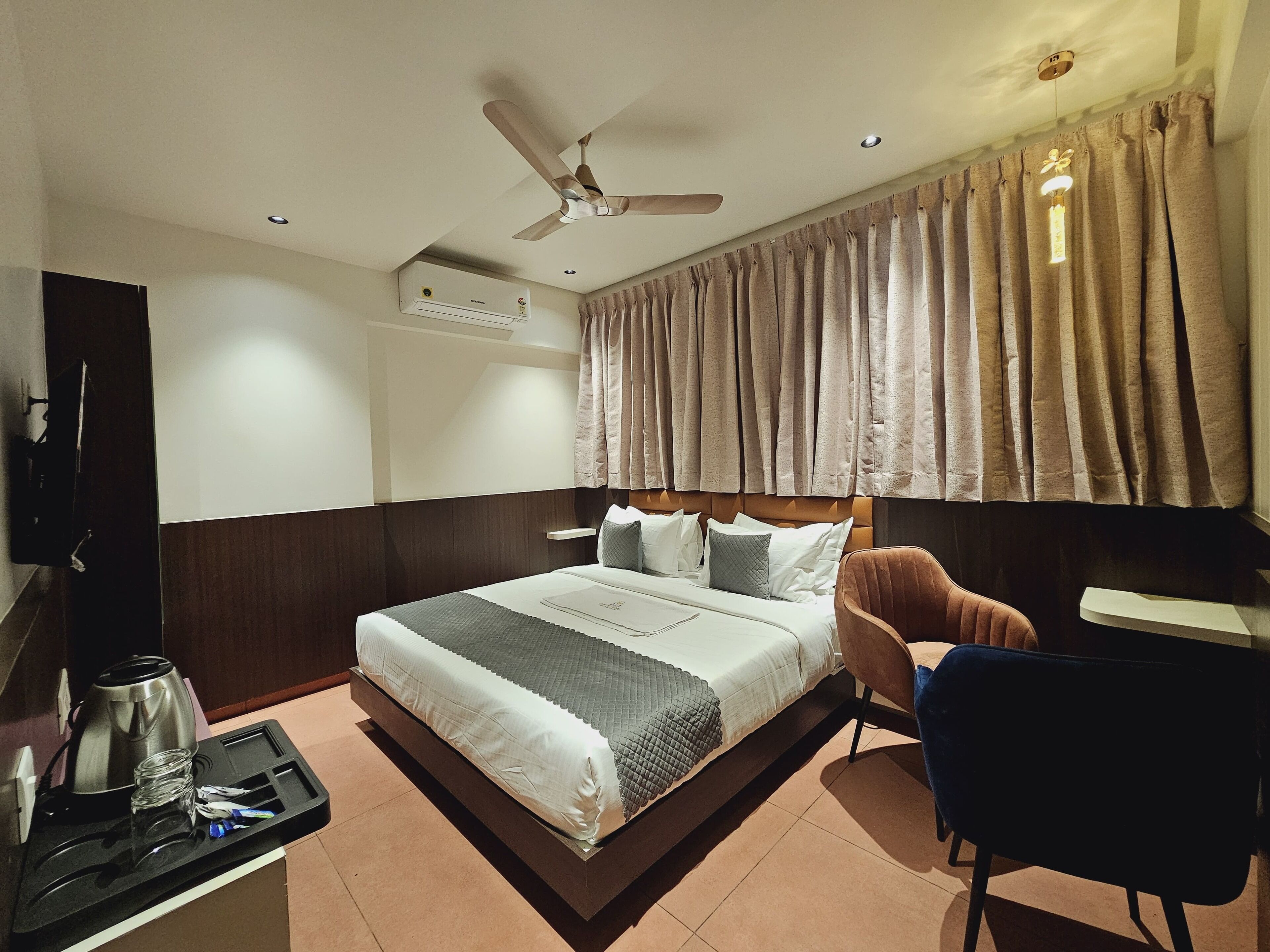 A hotel room with a bed, a desk, a chair, a coffee maker, and a ceiling fan.