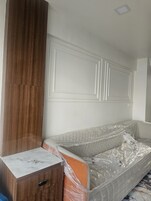 Quarto com guarda-roupa de madeira, cama coberta com plástico e cabeceira branca.