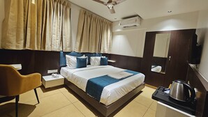 Ein Hotelzimmer mit einem Bett, einem Sessel, einem Schreibtisch mit Wasserkocher, einem Telefon und einem Deckenventilator.