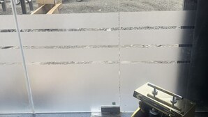 Blick aus einem Fenster mit einem Metallgitter, ein kleiner Tisch mit einem schwarzen Gegenstand und ein gefliester Boden.
