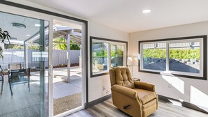 Een moderne woonkamer met een schuifdeur naar een terras, een leren fauteuil en grote ramen met uitzicht op groen.