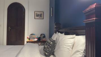A bedroom with a large bed, a wooden door, a small table with a coffee maker, and a framed picture on the wall.