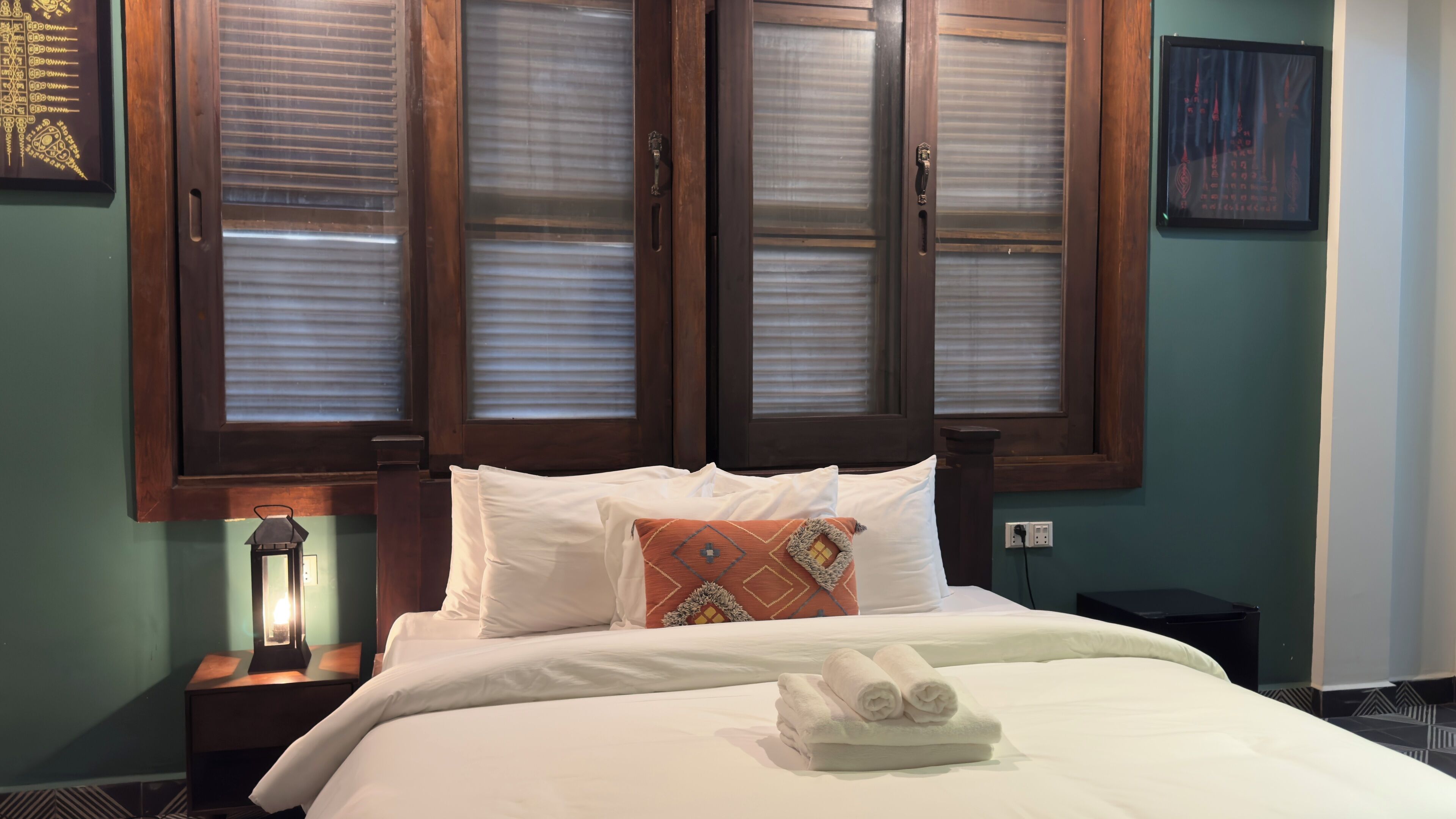 Cama bem arrumada com lençóis brancos e um travesseiro decorativo, abajur de cabeceira e quadro na parede.