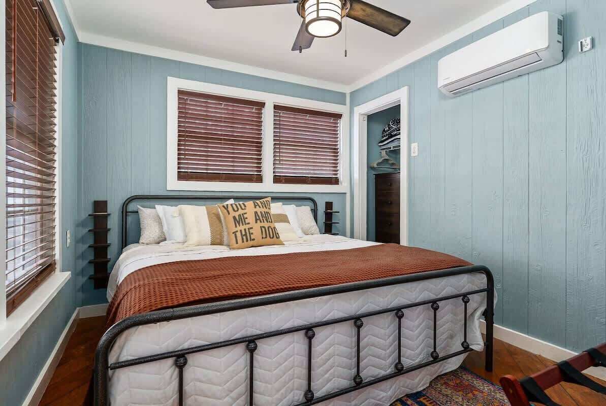 Ein Schlafzimmer mit einem Bett, einem Deckenventilator, einem Fenster mit Jalousien und einer Klimaanlage.