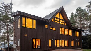 Ein modernes Holzhaus mit großen Fenstern, einem geneigten Dach und einer kleinen Terrasse.