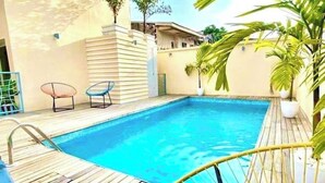 A swimming pool with a wooden deck, two lounge chairs, and a potted plant. - African Home Savane  (Douala)