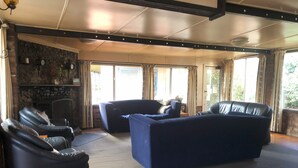 A spacious living area with leather sofas, a stone fireplace, and large windows offering a view of the outdoors.