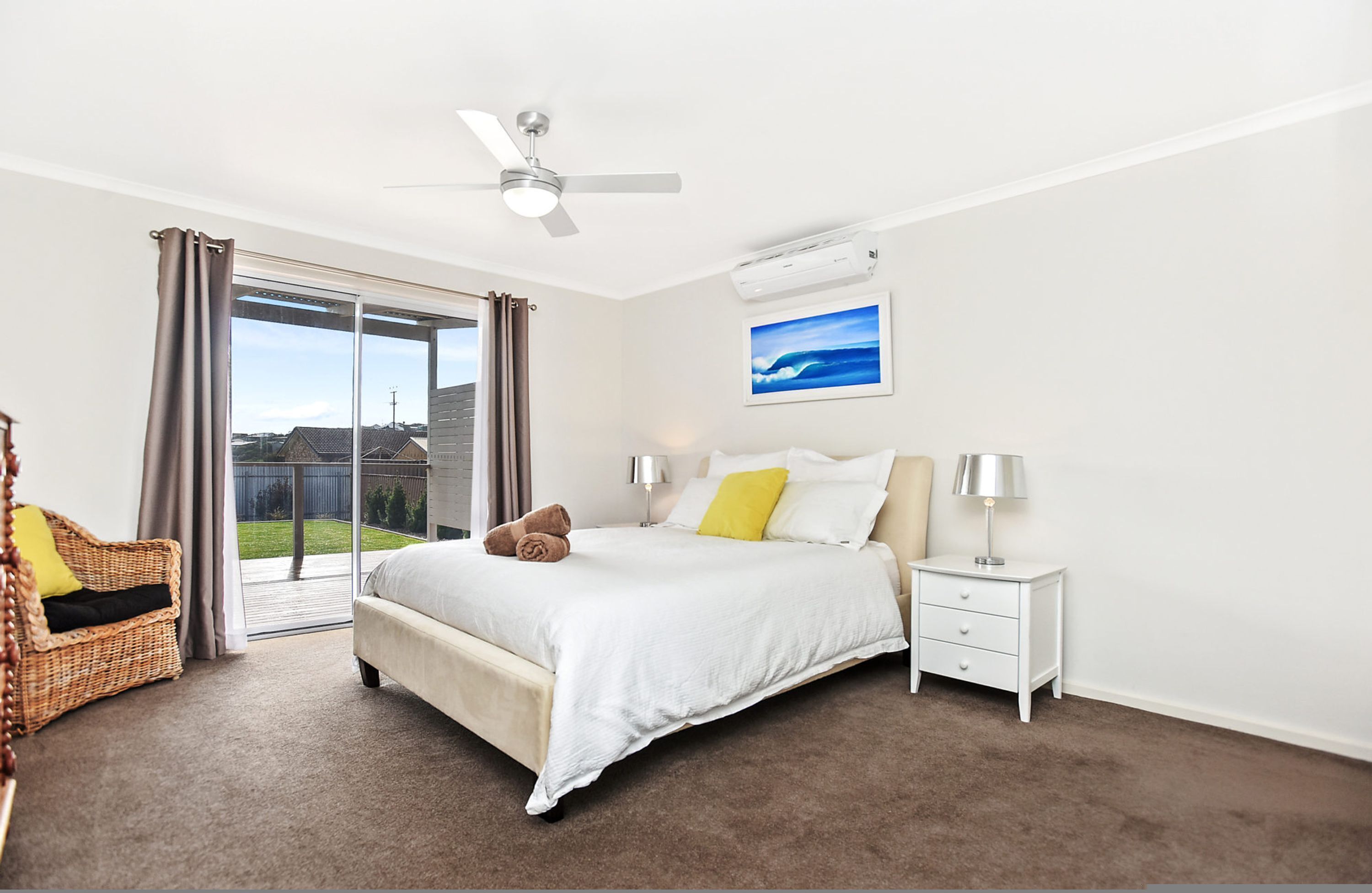 A bedroom with a bed, nightstands, a ceiling fan, and a view through a sliding glass door.