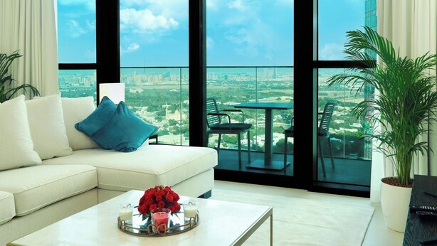 Uma sala de estar moderna com um sofá branco, uma mesa de centro com uma bandeja de rosas vermelhas e vista para um horizonte urbano por grandes janelas.