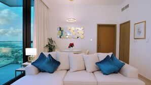 Une chambre d’hôtel moderne avec une grande fenêtre, un canapé avec des coussins bleus, une table ronde ornée d’un vase de fleurs et un élément décoratif mural.