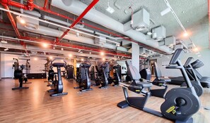 A gym with various exercise equipment, wooden flooring, and exposed pipes on the ceiling.