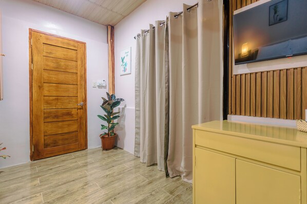 Un couloir avec une porte en bois, une plante en pot, un rideau et un téléviseur fixé à un mur en bois.