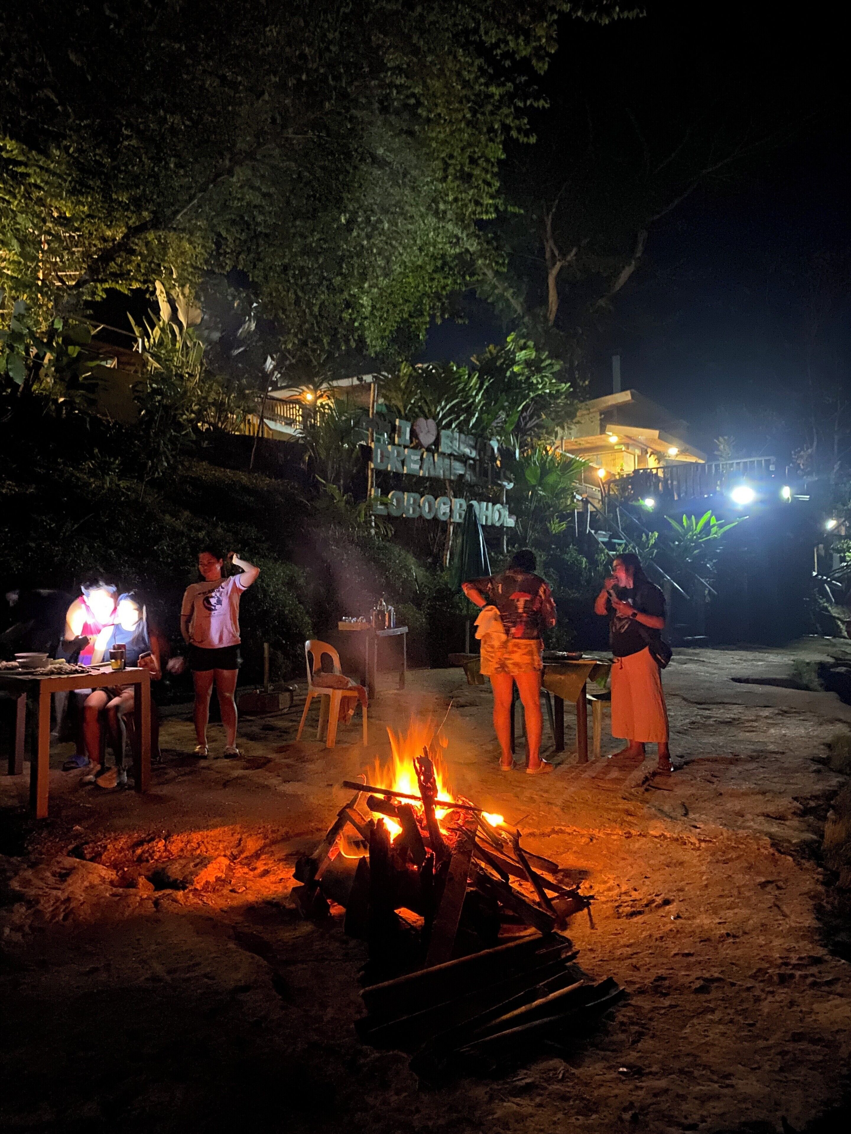 Ein Treffen im Freien mit Lagerfeuer, einem Schild und einem Tisch mit Stühlen.