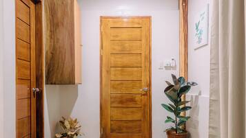 A hallway with a wooden door, potted plants, and a tiled floor.