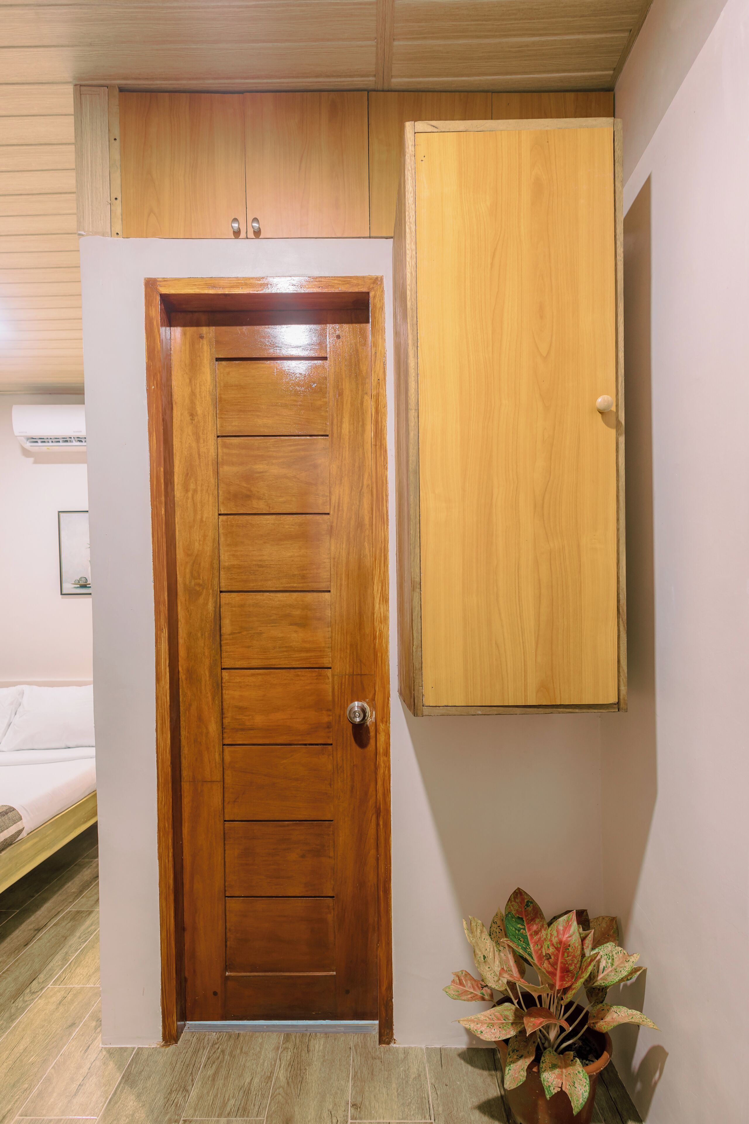 Une porte en bois avec une poignée, un petit meuble fixé au-dessus, et un pot de fleurs placé à côté de la porte.
