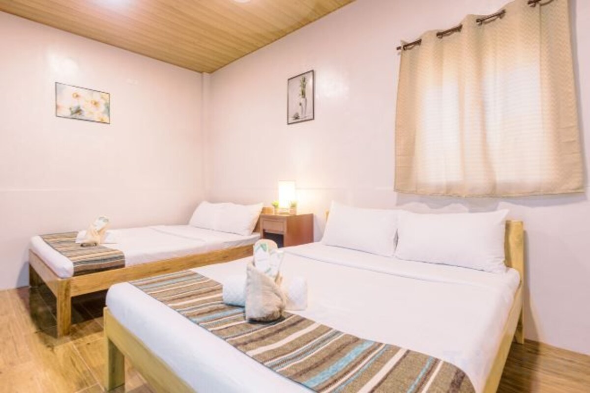A hotel room with two single beds, wooden headboards, a nightstand with a lamp, and a window with curtains.