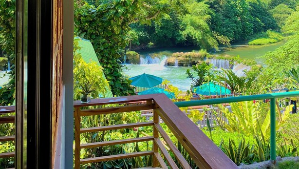 A wooden balcony with a woven ceiling, overlooking a lush green landscape with a waterfall. - BUSAI DREAM FALLS RESORT (Sevilla)