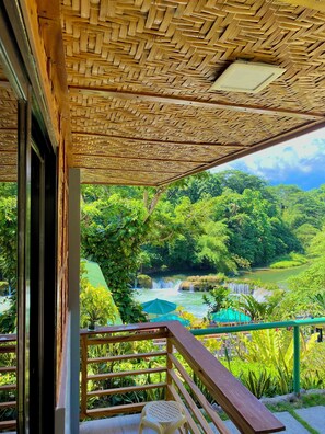 A wooden balcony with a woven ceiling, overlooking a lush green landscape with a waterfall. - BUSAI DREAM FALLS RESORT (Sevilla)