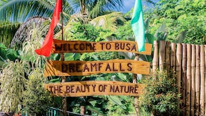 A wooden sign with flags and text welcoming visitors to Busa, highlighting the beauty of nature. - BUSAI DREAM FALLS RESORT (Sevilla)