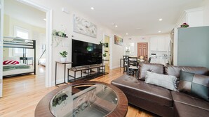 Ein modernes Wohnzimmer mit einem braunen Ledersofa, einem Glastisch, einem Flachbildfernseher und einem Essbereich mit einem Holztisch und Stühlen.