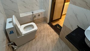 A compact bathroom with a toilet, a small sink, and a shower area. - The Kashi Yatra Inn (Varanasi)