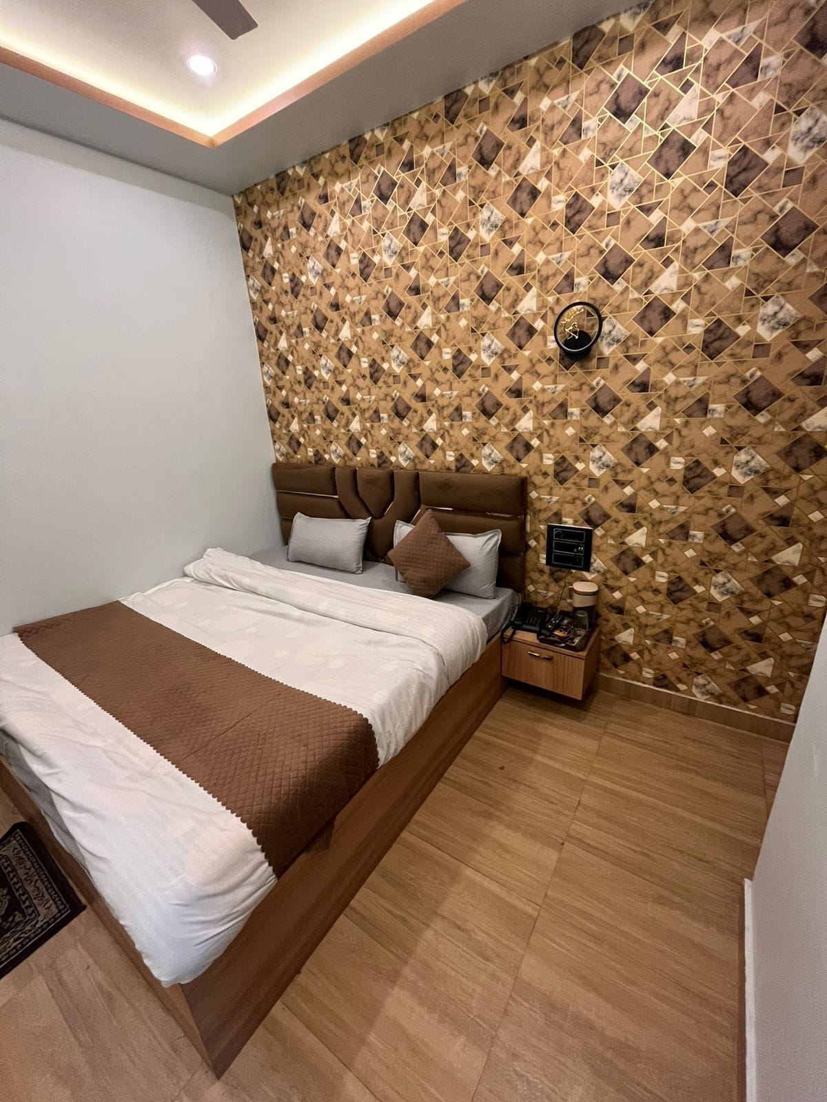 A modern bedroom with a geometric patterned wall, a wooden bed frame, and a bedside table with a lamp.