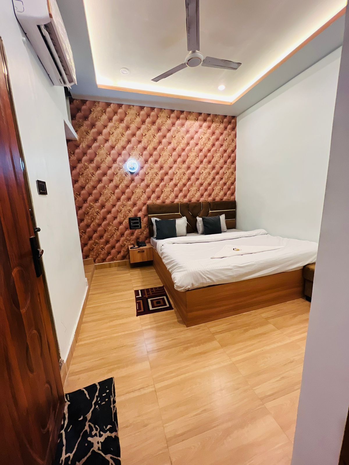 A bedroom with a wooden bed, a ceiling fan, a patterned wall, and a small bedside table.