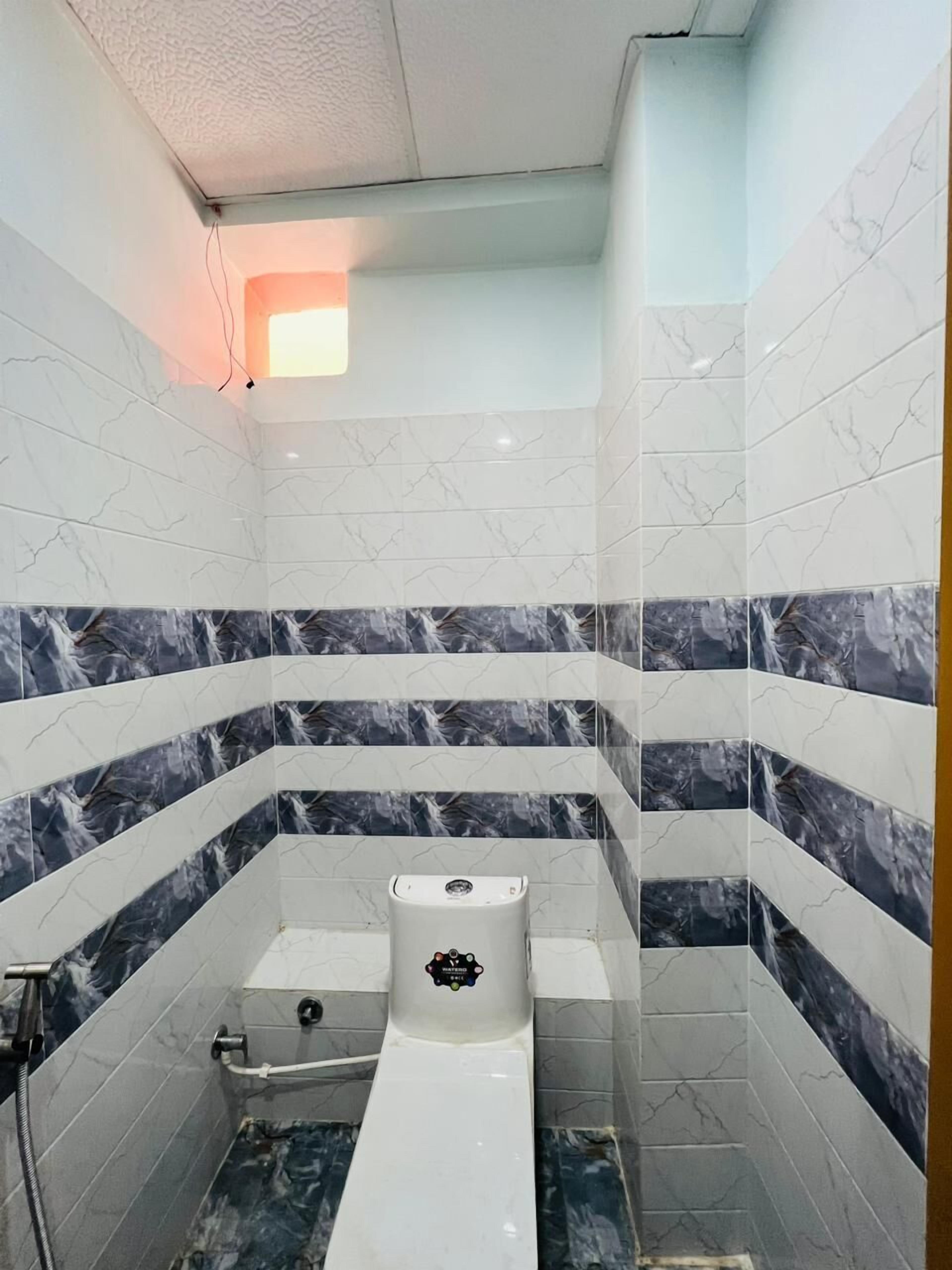 A bathroom with white and marble-patterned tiles, a white toilet, and a shower area.