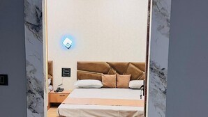 A bedroom with a bed, nightstand, and wall-mounted phone. - The Kashi Yatra Inn (Varanasi)