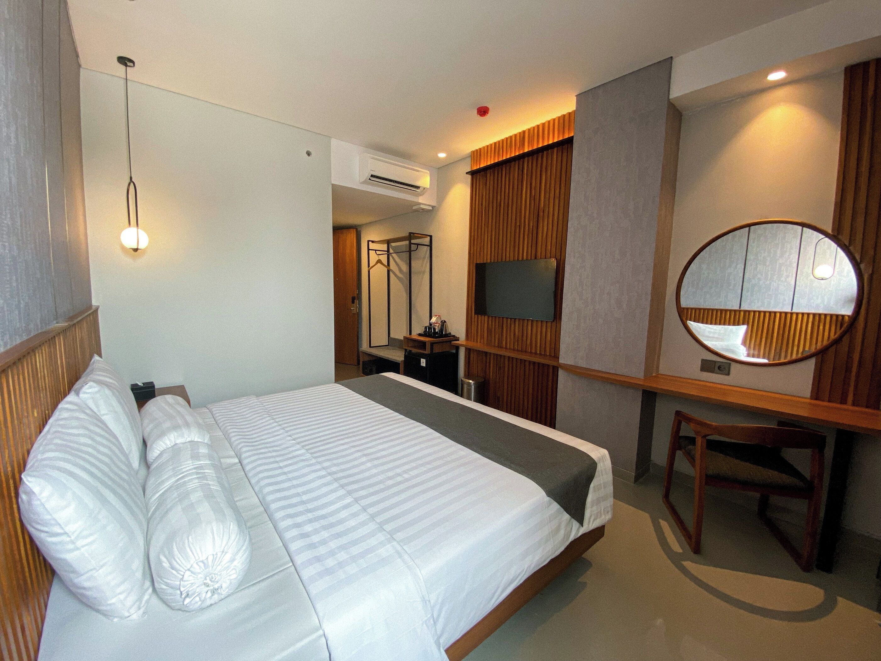 Habitación de hotel con cama, escritorio, silla, espejo y televisor.