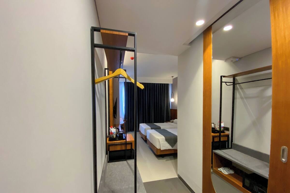 A modern hotel room with a large mirror, a bed, a bedside table, and a wardrobe.